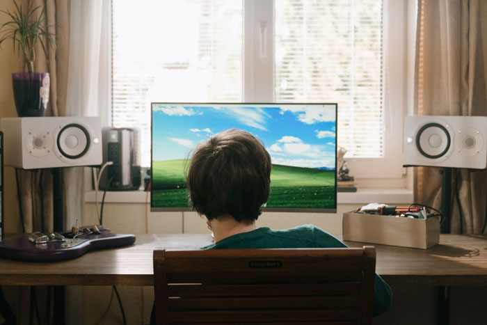 Child facing computer screen displaying most viewed photo ever hill scenery Child facing computer screen displaying most viewed photo ever hill scenery