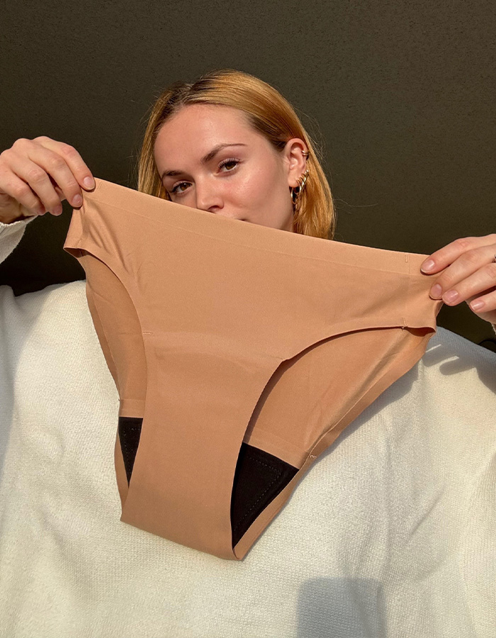 Woman holding brown period underwear against dark background