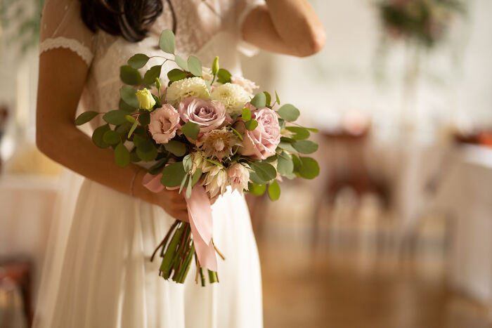 Bride holding a pastel floral bouquet in wedding dress indoors