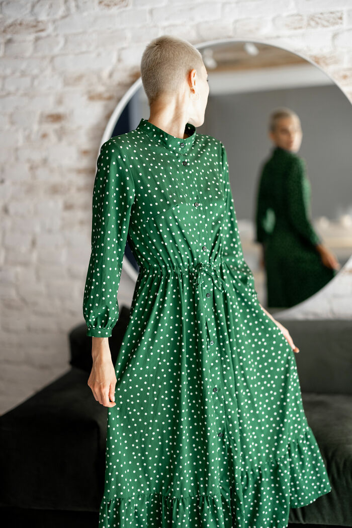 Person in green polka dot dress looking at reflection in mirror indoors