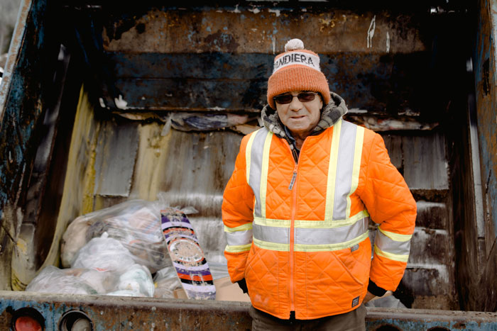 Garbage collector in bright orange jacket and beanie by rubbish truck Garbage collector in bright orange jacket and beanie by rubbish truck