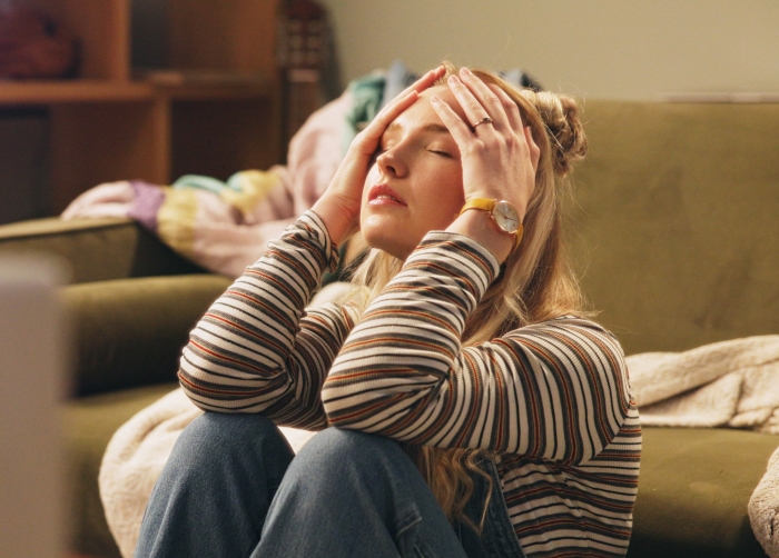Woman sitting on floor, stressed and holding her head in anxiety inside a living room