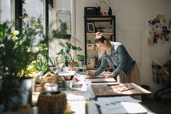 A woman drawing at a desk, surrounded by plants. AI has already axed jobs worldwide, but some careers are safe.