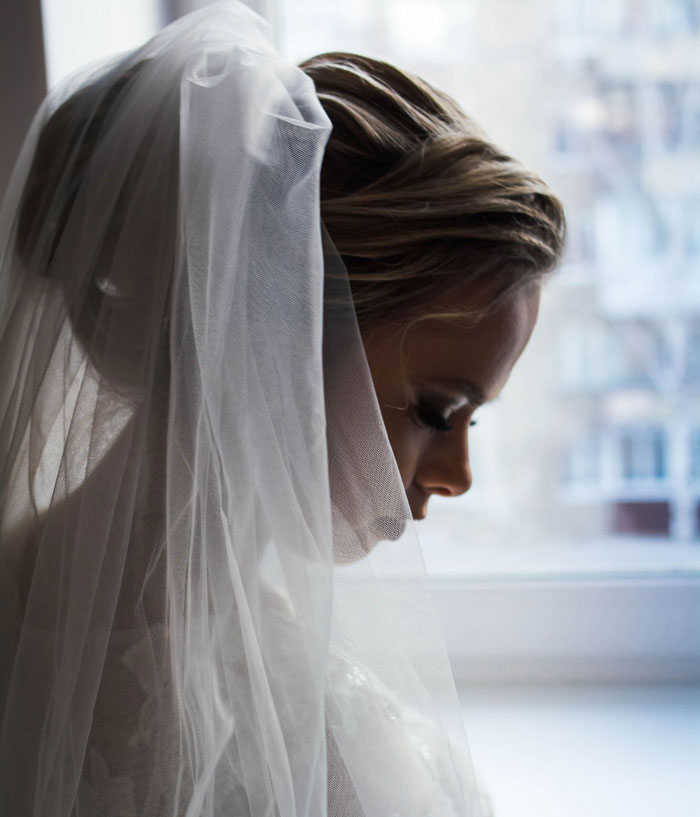 A sad bride in a wedding veil looking down, holding back tears on her wedding day.