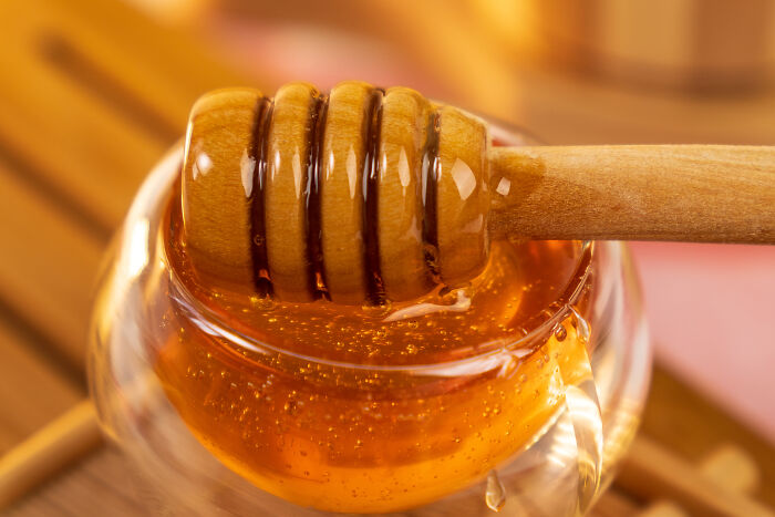 A close-up of a honey dipper in a glass jar of golden honey, illustrating useless facts.