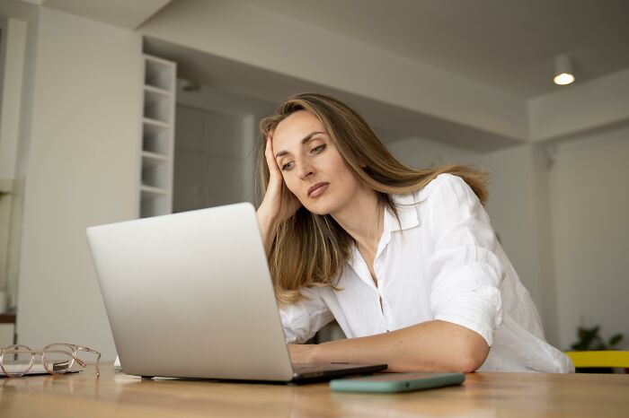 A tired woman teacher looking at her laptop, probably reading a message from entitled parents.
