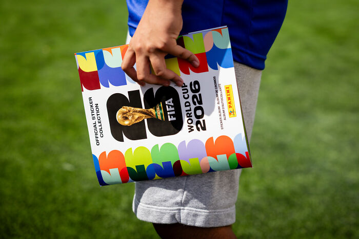 Person holding official FIFA World Cup 2026 sticker album outdoors