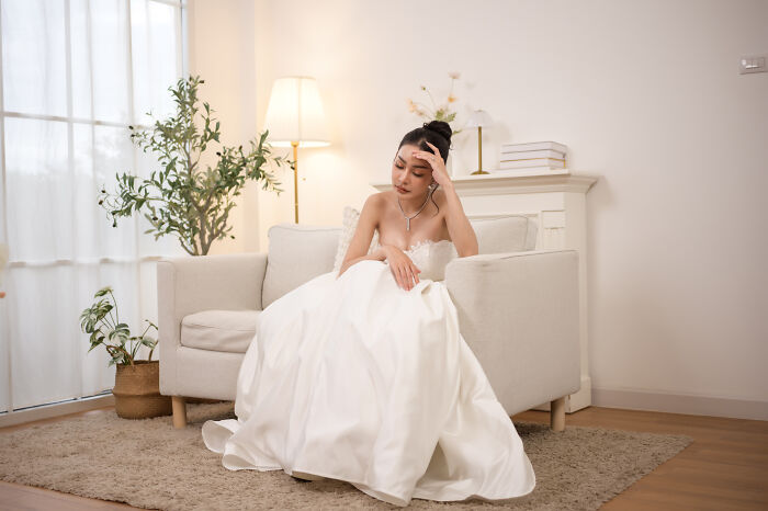 Upset bride sitting on couch in wedding dress feeling stressed