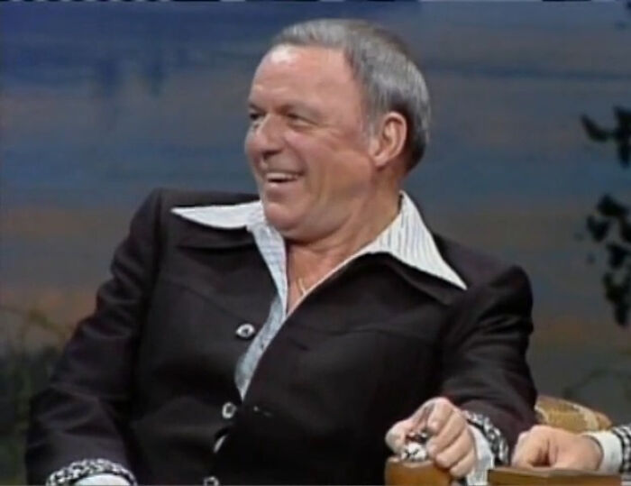 Smiling older man in black suit recalling celebrity meetings