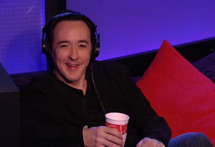 Smiling celebrity sitting with headphones holding a cup during an interview about celebrity encounters