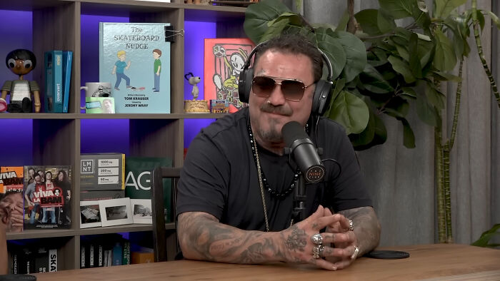Tattooed man speaking into microphone in podcast studio about celebrity encounters
