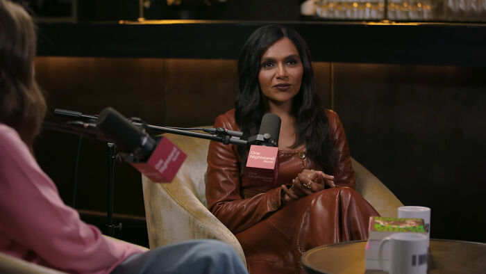 Woman in brown leather outfit speaking on podcast about celebrity encounters