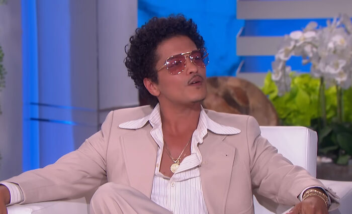 Man wearing retro suit and glasses discussing celebrity stories