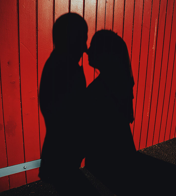 Silhouetted couple kissing against a bright red wall background