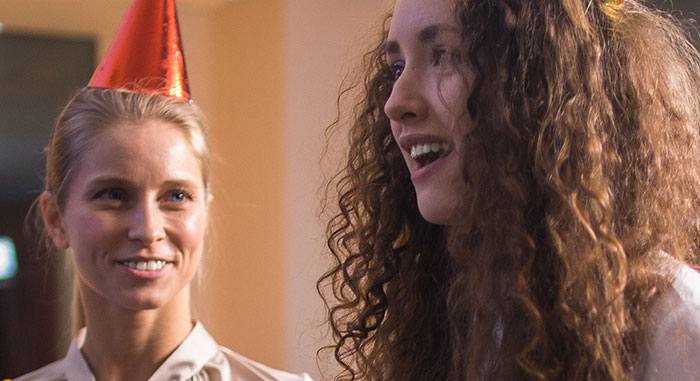 Two women at party with one wearing a birthday hat representing fired employees