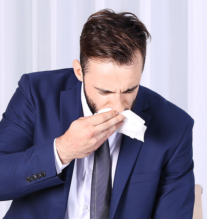 Businessman sneezing at work symbolizing fired employees