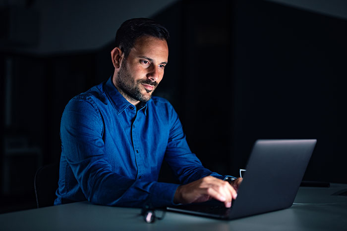 Man working late on laptop in dark office representing fired employees