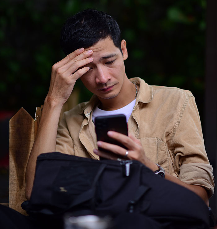 Worried man looking at phone with hand on forehead outdoors