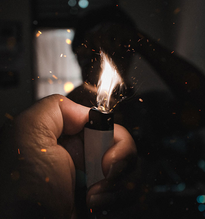 Hand lighting a lighter with silhouette figure in background symbolizing friend moments