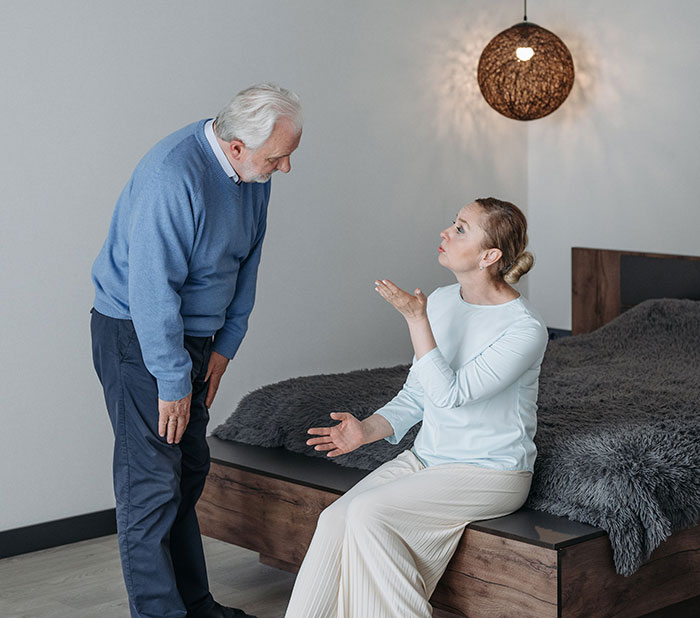 Older man and younger woman having serious conversation in bedroom