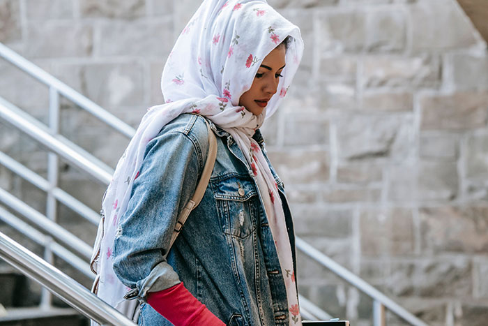Woman wearing floral headscarf and denim jacket walking down stairs thinking about friendship