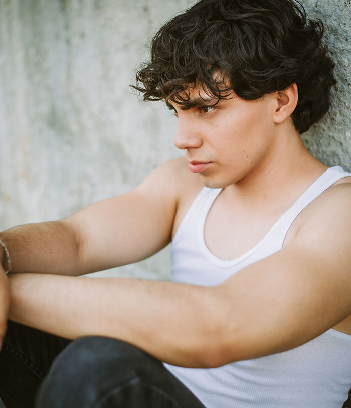 Pensive young man sitting alone leaning on wall lost in thought
