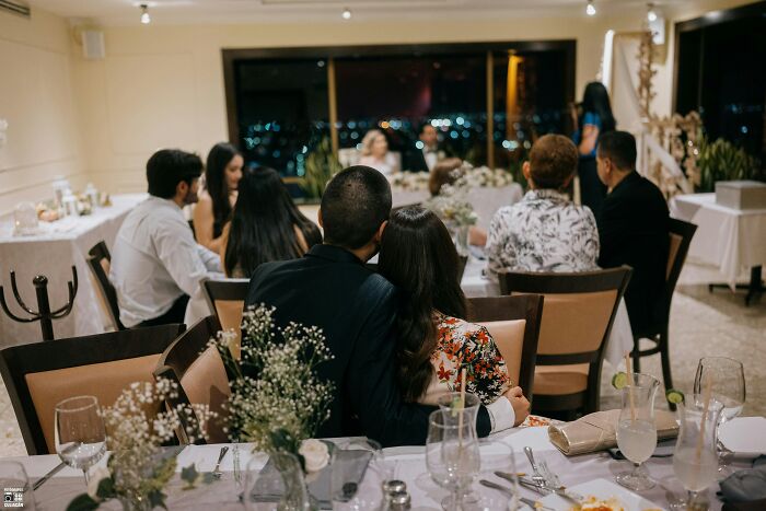 Couple sitting and embracing at a wedding reception table with guests