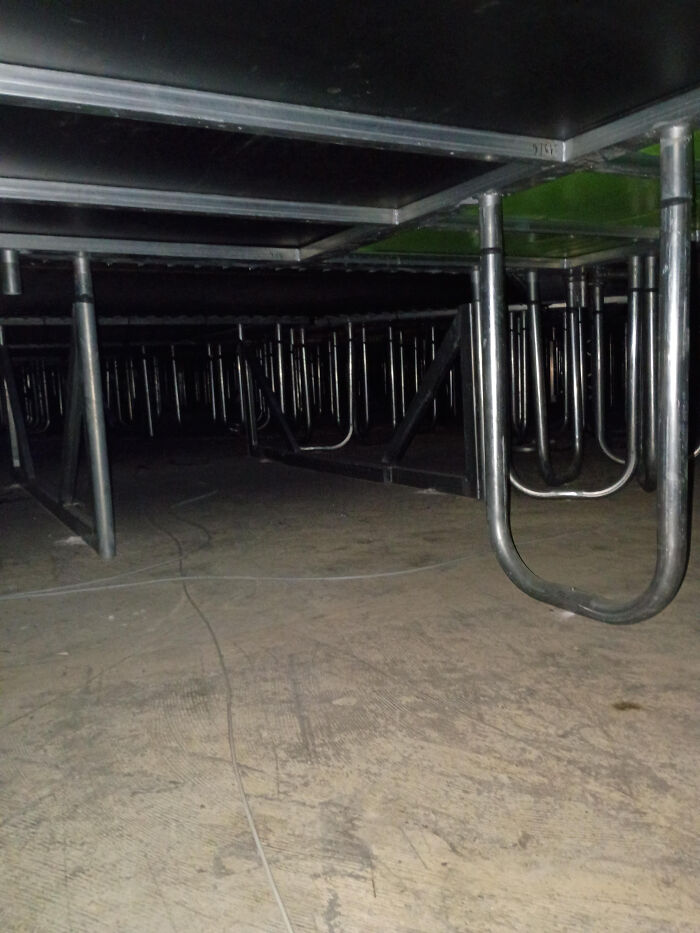 An unsettling view beneath a stage structure, revealing a hidden, dark liminal spaces with metal supports and wires.