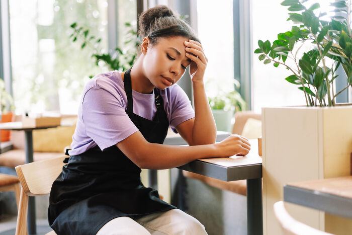 A waitress in an awkward situation, holding her head, looking tired in a cafe.