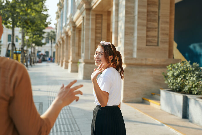 A young woman smiles and waves while visiting the US, engaging with local culture and experiences.