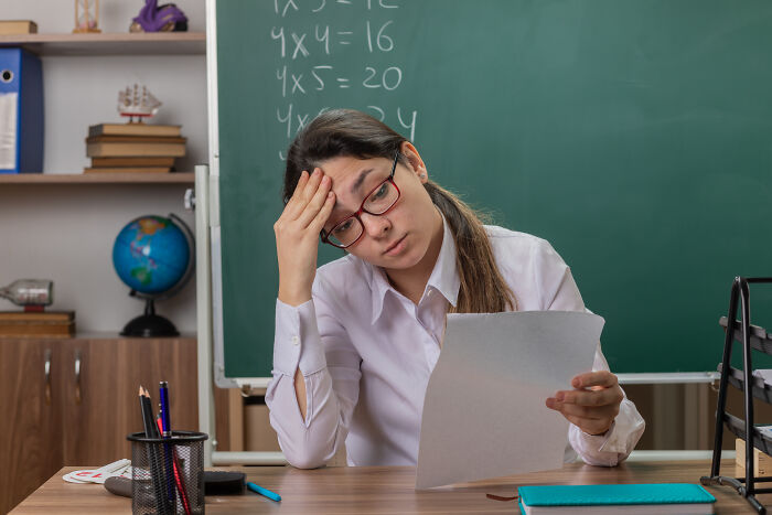 A stressed teacher in a classroom, looking at a message from entitled parents.