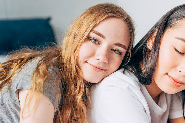 A woman smiling while her sister rests her head on her shoulder. The sisters are close. A woman smiling while her sister rests her head on her shoulder. The sisters are close.