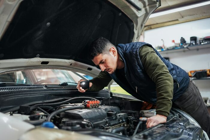 Man inspecting car engine with flashlight in repair shop modern world audacity