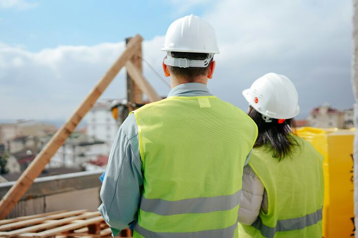Two construction workers wearing hard hats and safety vests, not directly related to women who marry their partner.