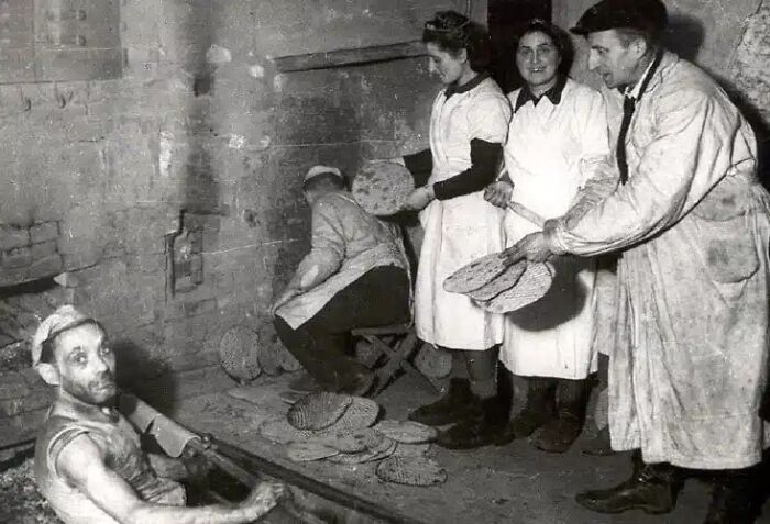 Workers in a historical photo are seen baking bread in an old oven, a scene from impossible to explain historical photos.