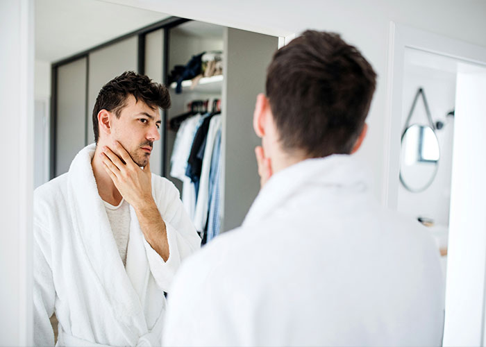 A man in a white robe looking at himself in the mirror. This relates to men and their worst selves.