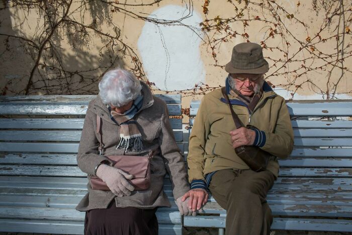 Elderly couple holding hands on a bench, a serendipitous moment captured in everyday life by a street photographer.