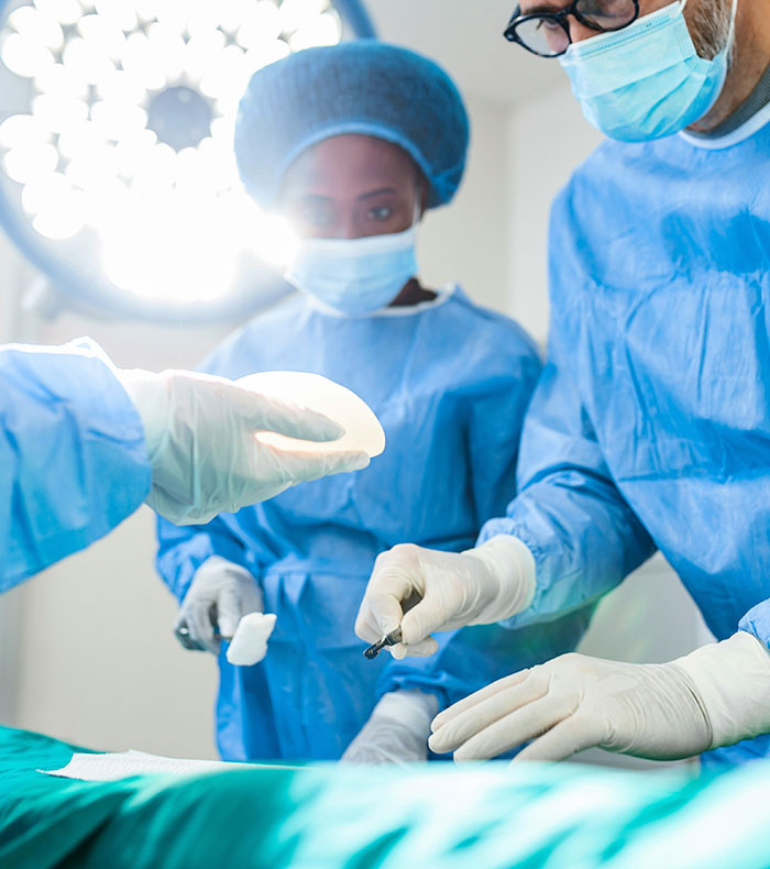 Doctors during a breast implants removal surgery, with one holding a saline implant. Doctors during a breast implants removal surgery, with one holding a saline implant.