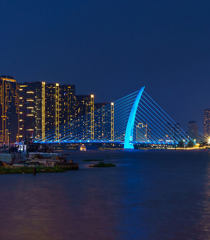 A river at night, with a modern bridge illuminated in blue and buildings with yellow lights in the background. A river at night, with a modern bridge illuminated in blue and buildings with yellow lights in the background.