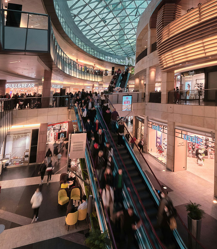 A busy shopping mall with many people on escalators, depicting a public setting for potential public shaming. A busy shopping mall with many people on escalators, depicting a public setting for potential public shaming.