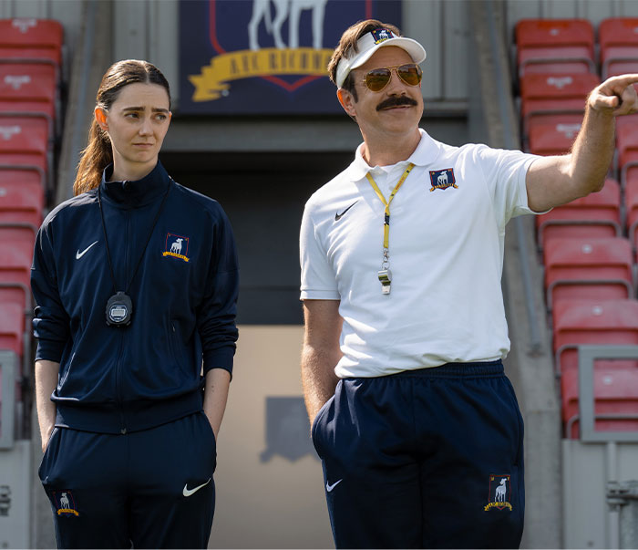 Ted Lasso and a female coach on the field, calling out heavy photoshop in beauty standards.