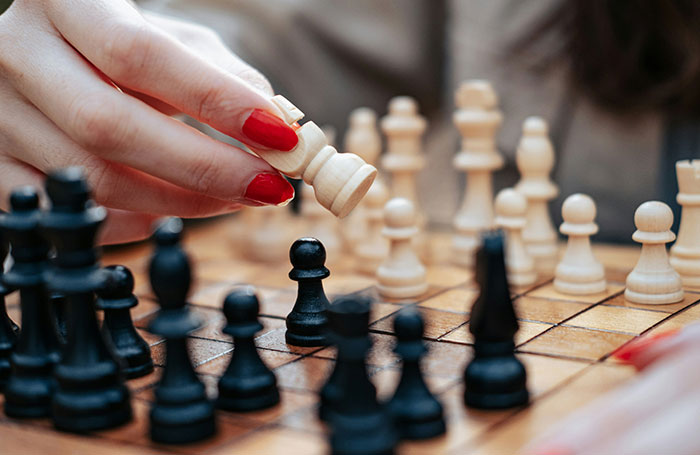 A close-up of a female hand with red nails moving a chess piece during a game, highlighting the chess community. A close-up of a female hand with red nails moving a chess piece during a game, highlighting the chess community.