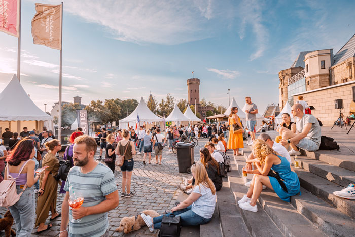 A vibrant outdoor festival with many people, food stalls, and tents under a bright sky, relating to the Karen story.