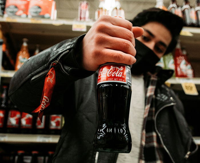 A person in a black jacket and face mask holding a Coca-Cola bottle in a store, central to the Karen story.