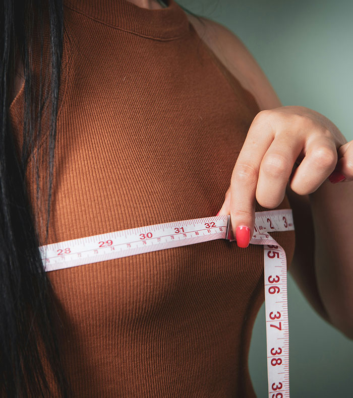 A woman measures her breast, revealing the size of her painful breast implants. A woman measures her breast, revealing the size of her painful breast implants.