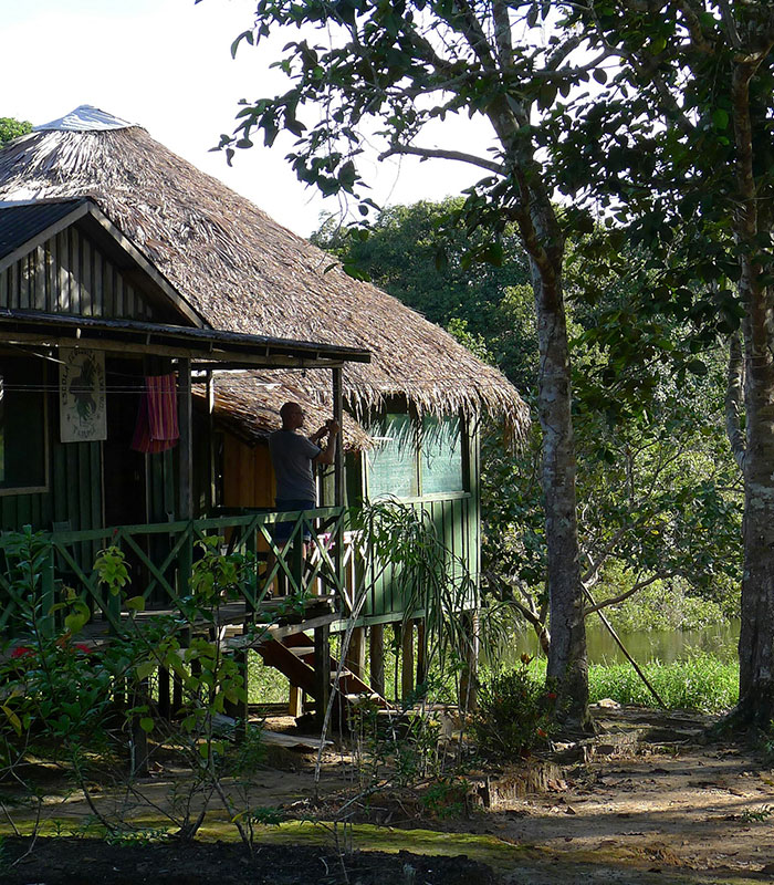 A man on the porch of a hut in an Amazonian remote tribe village, nestled among trees by a river. A man on the porch of a hut in an Amazonian remote tribe village, nestled among trees by a river.