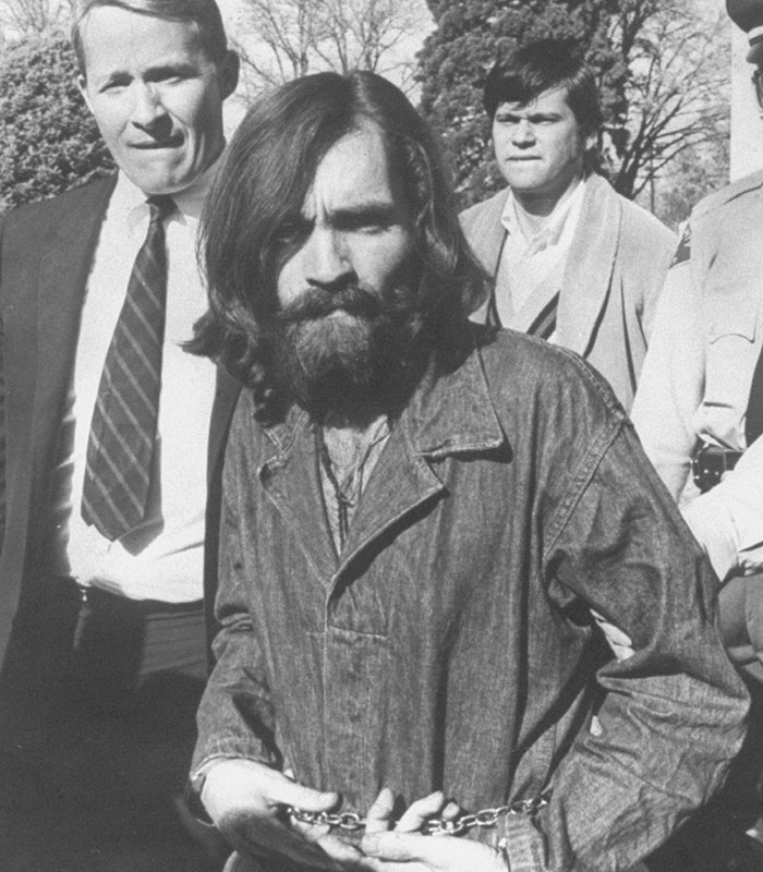 Charles Manson in chains being escorted by men, revealing eerie similarities with a woman's dad. Charles Manson in chains being escorted by men, revealing eerie similarities with a woman's dad.