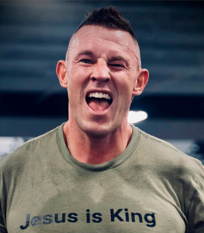 A Christian man in a men-only gym wearing a Jesus is King shirt, smiling and winking.