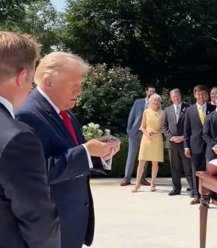Donald Trump holds an award he didn't win, surrounded by people outdoors. Donald Trump holds an award he didn't win, surrounded by people outdoors.