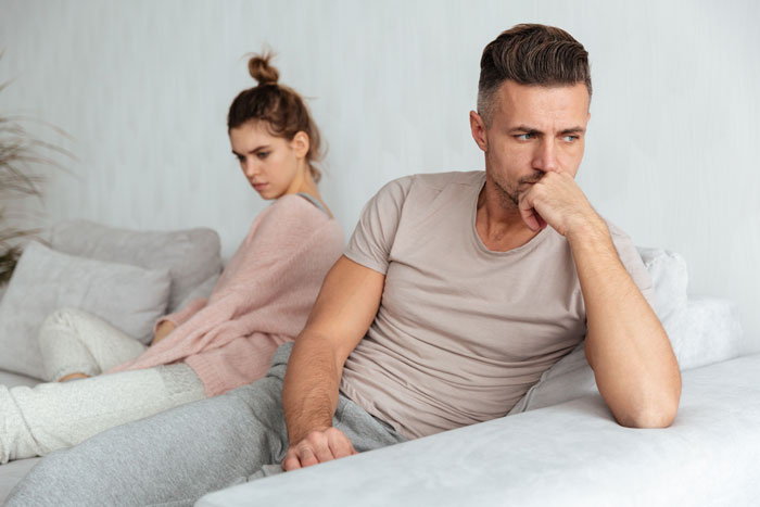A couple sits with their backs to each other on a sofa, looking upset due to the cheating wife and her affair. A couple sits with their backs to each other on a sofa, looking upset due to the cheating wife and her affair.